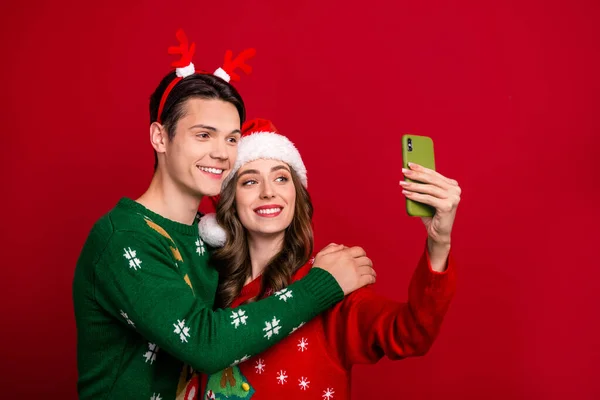Portrait of two peaceful cheerful people embrace hold telephone make selfie isolated on red color background.