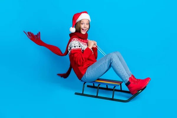 全长照片可爱兴奋的女生穿着红色圣诞装饰品套头衫骑着快雪橇孤立的蓝色背景 — 图库照片