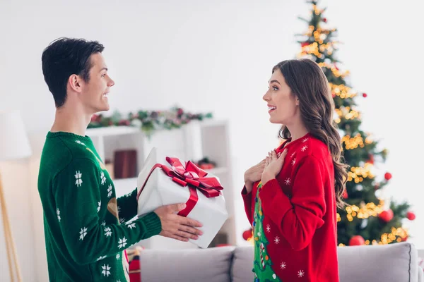 興奮した若いカップルの女性の写真は醜い赤いセーターを身に着けています驚きの手胸驚きの贈り物からサンタクラスショッピングプロモーション屋内 — ストック写真