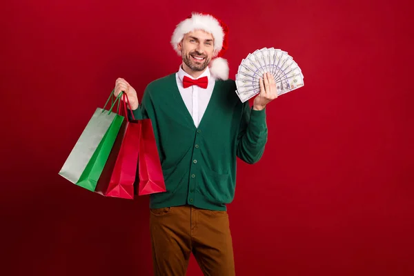 満足豊かな手入れの行き届いた男の写真サンタクラスの帽子素敵な蝶ネクタイは多くのお金を保持スタックショッピングバッグは赤の色の背景に隔離 — ストック写真