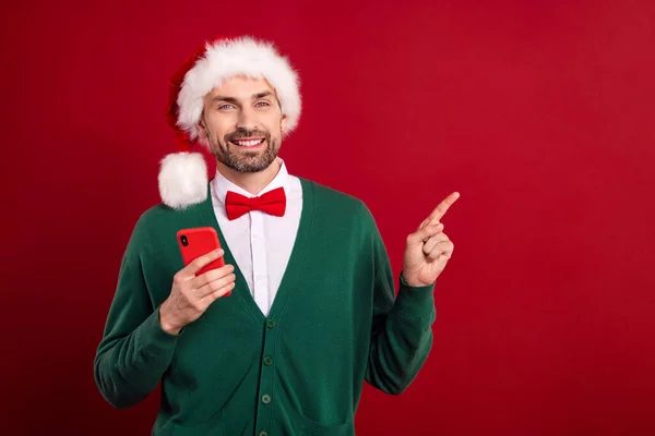 若い自信に満ちた紳士の写真クリスマスの雰囲気は 赤い色の背景に隔離された電話ショッピングプロモーションの指を直接モックアップを保持帽子を着用 — ストック写真