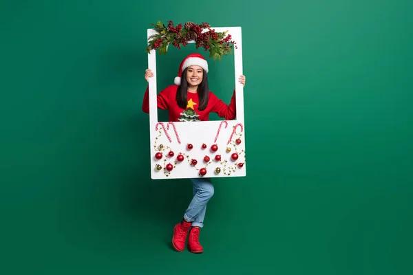 甜美可爱的女士身穿红色丑陋印花圣诞毛衣 手持装饰白色相框 绿色背景的全长照片 — 图库照片
