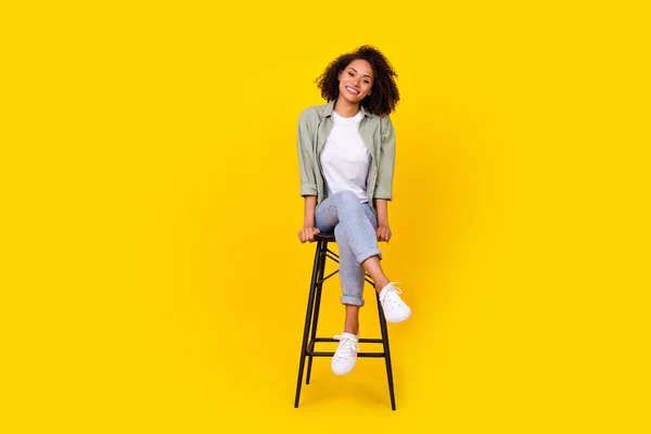 全身上下都是快乐的年轻女子卷发坐在椅子上闲聊的照片 穿着时髦的卡其布套装 与黄色背景隔离 — 图库照片