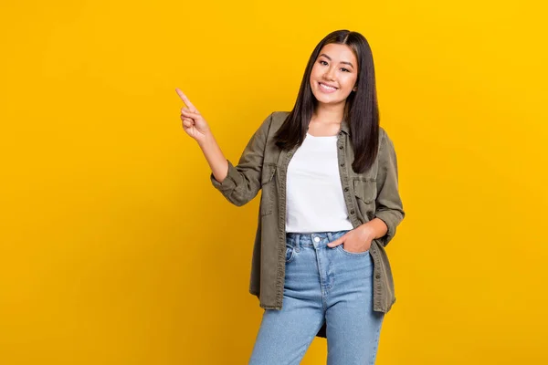 Stock image Portrait of good mood girl with long hairstyle dressed khaki shirt arm in pocket directing empty space isolated on yellow color background.