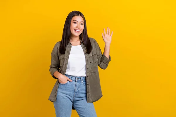 stock image Portrait of good mood satisfied nice girl long hairdo wear khaki shirt hold arm in pocket waving hand isolated on yellow color background.