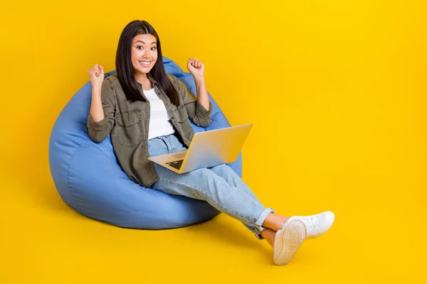 若い開発者のラップトップのフルボディサイズの写真日本の女性は座って快適なビーンズバッグは黄色の背景に隔離された最初のプロジェクトを祝う — ストック写真