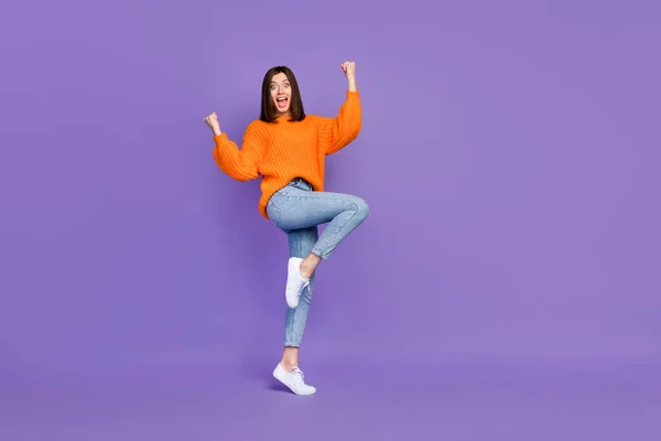 素敵な若い女性のフル長さの写真を上げる拳を獲得宝くじ服スタイリッシュなオレンジニット服紫色の背景に孤立 — ストック写真