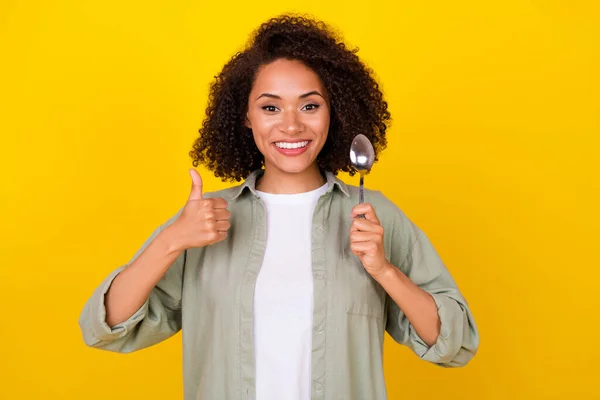 写真のファンキーな巻きミレニアルブルネットの女性食べる食べ物親指アップ着用グレーシャツ隔離された黄色の色の背景 — ストック写真
