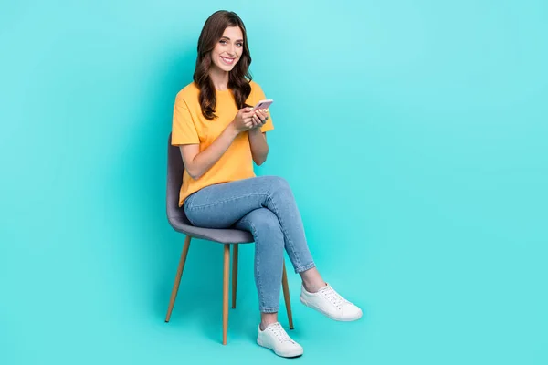 かわいい甘い女性の完全な長さの写真は黄色のTシャツタイプ現代的なデバイス空のスペース座って椅子隔離されたターコイズ色の背景 — ストック写真