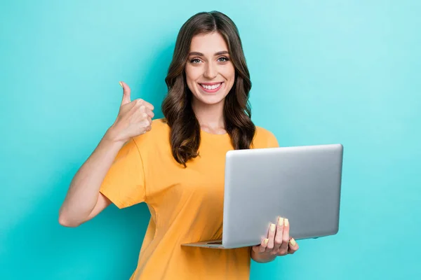 年轻漂亮迷人的女孩穿着黄色T恤 拿着笔记本电脑 很好的应用程序Facebook开发人员的合影 在青色背景下显示出孤立的大拇指 — 图库照片