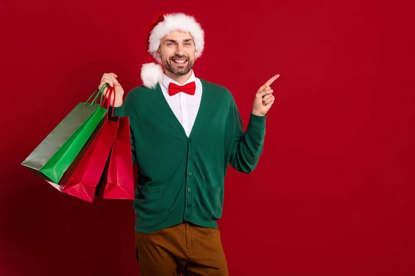 若いクリスマスの男の写真は お祝いの帽子素敵な居心地の良い服を保持スタックショッピングバッグ指直接空のスペースに隔離された赤の色の背景 — ストック写真