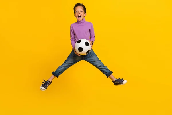 フルサイズの写真の喜びエネルギー少年ジャンプ手ホールドサッカー孤立した上の黄色の背景 — ストック写真