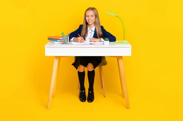 穿着蓝色夹克 一头直发的令人心满意足的女学生的画像 坐在书桌前 与黄色背景隔离 — 图库照片