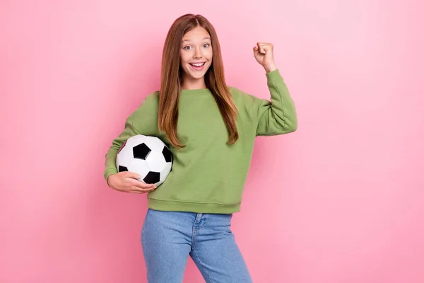 照片上漂亮的幸运女学生穿着绿色运动衫拿着足球上升的拳头孤立的粉色背景 — 图库照片