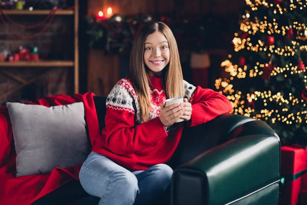 明るい女の子の肖像座ってソファの手を保持コーヒーマグカップツリーガーランドライトハウス屋内 — ストック写真
