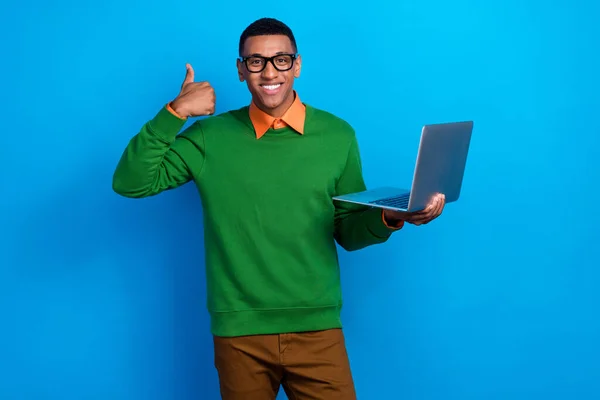 绿色套头衫下乐观的好心情男人橙色衬衫的画像 手持笔记本电脑 在蓝色背景下显示出孤立的大拇指 — 图库照片