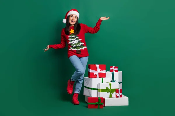 照片全长可疑女士身穿红色丑陋印花圣诞毛衣举起双手礼品堆叠孤立的绿色底色 — 图库照片