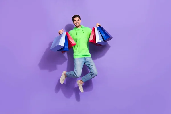 全长照片 照片上穿着霓虹灯运动衫的可爱男子跳上高耸的购物者孤立的紫罗兰色背景 — 图库照片