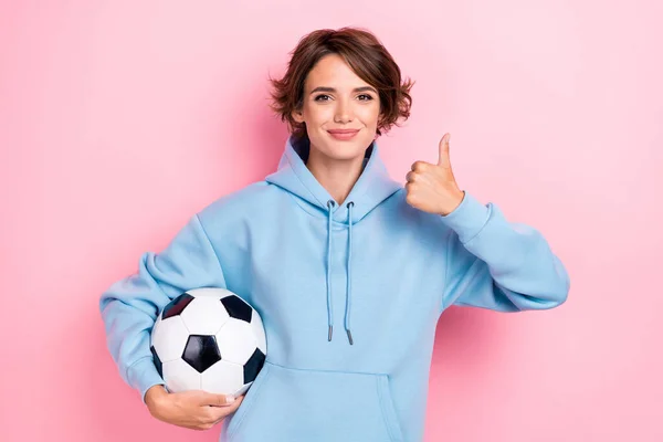若いです魅力的な女の子の写真かなり素敵な女性着用青パーカーホールドサッカーボールファンショーのような親指アップ絶縁上ピンク色の背景 — ストック写真