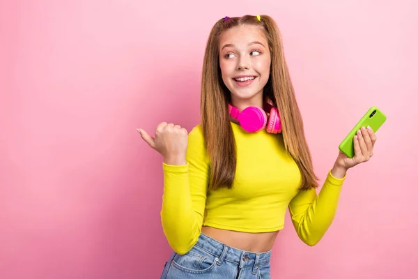 楽観的な関心のある女の子の写真黄色のトップヘッドフォンは 黄色の色の背景に隔離された空のスペースに見える電話を保持 — ストック写真