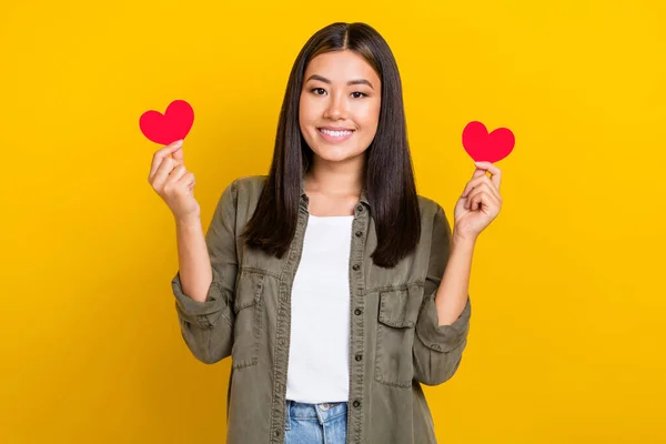 若い笑顔ベトナムの女の子の写真は 黄色の色の背景に隔離された赤の愛のシンボルバレンタインデーを保持Kakiトレンディーなシャツブルネットの髪を身に着けている — ストック写真