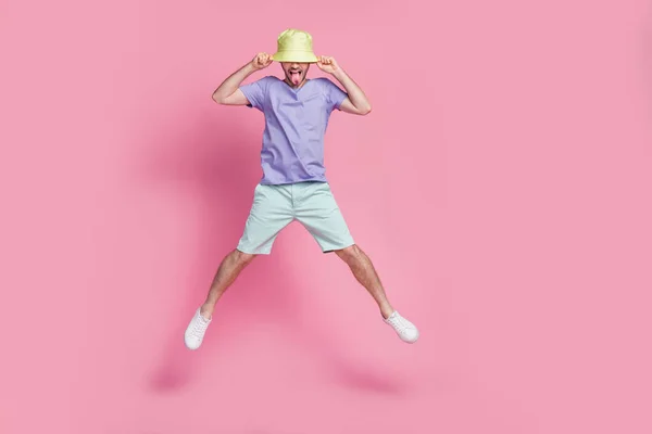魅力的な若い男のジャンププル帽子舌アウト広がる足服トレンディーな青の衣装ピンク色の背景に隔離された — ストック写真
