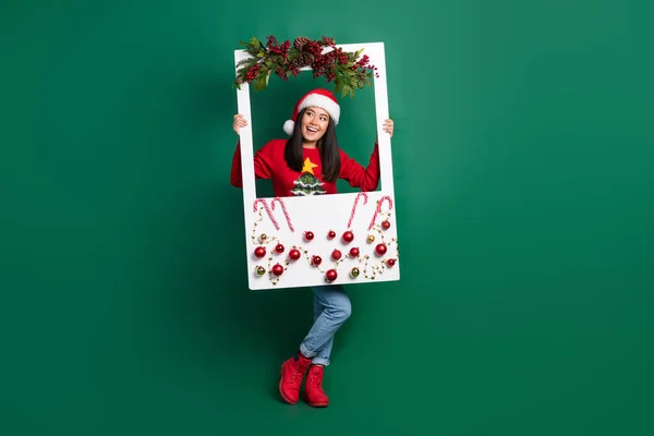 全长照片 漂亮的梦幻女郎穿着丑陋的印花红色圣诞套头衫升挂装饰窗台空旷的空间孤立的绿色背景 — 图库照片