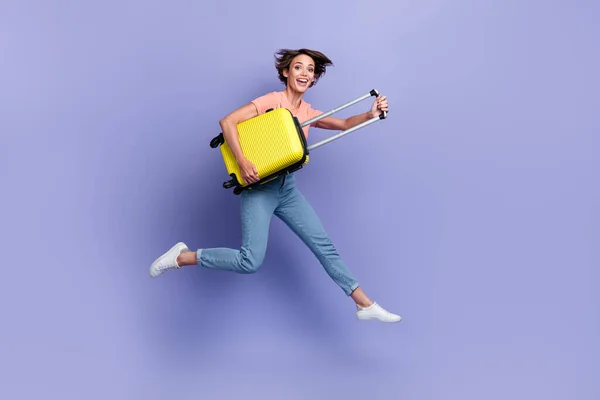 stock image Full length photo of sweet excited girl dressed orange t-shirt jumping high holding suitcase isolated purple color background.