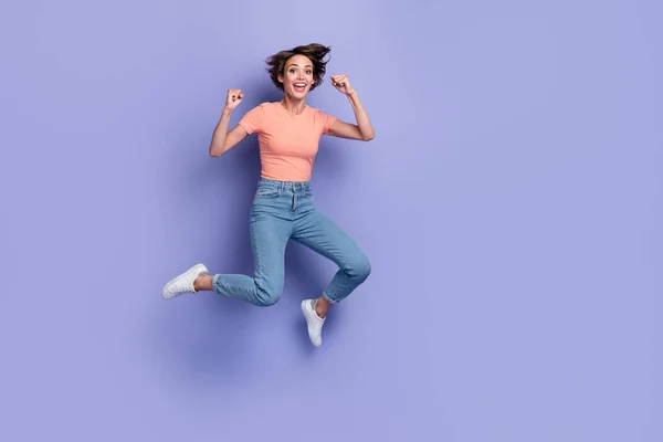 フル長さ写真の愛らしい運の良い女性の着用ストライプTシャツジャンプ高い上昇拳空のスペース隔離された紫色の背景 — ストック写真