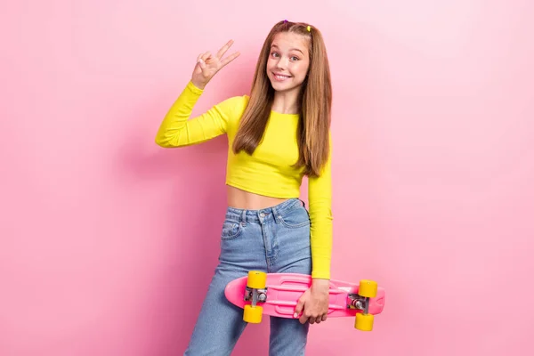 可爱迷人的女学生穿着黄色作物顶部骑长板的照片 显示V字形孤立的粉色背景 — 图库照片