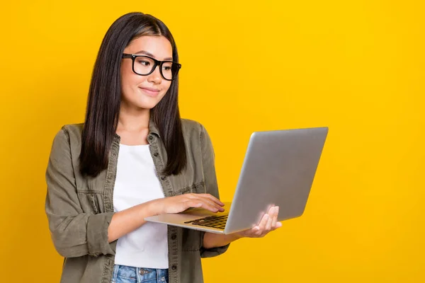 照片上积极快乐的聪明女孩 一头乌黑的头发 穿着灰色衬衫 写着电子邮件 手持笔记本电脑 与黄色背景隔离 — 图库照片