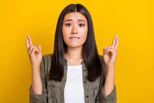 Portrait photo of young nervous grimace chinese woman wear khaki shirt bite lips nervous wish best exam result isolated on yellow color background.