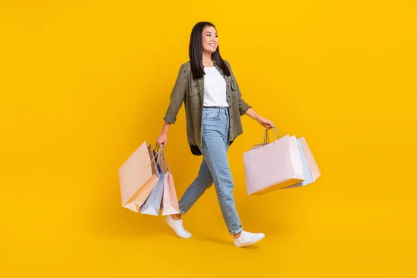 フルボディ写真の若い正の良い気分服デザイナー韓国の女の子ホールドパッケージからショッピング歩行ブティック隔離された黄色の色背景 — ストック写真