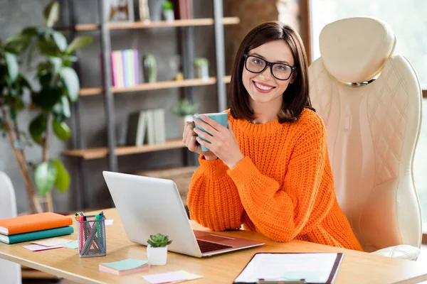 快乐微笑的女士穿着橙色毛衣工作在现代化设备上享受喝茶休息放松室内车间工作站的照片 — 图库照片