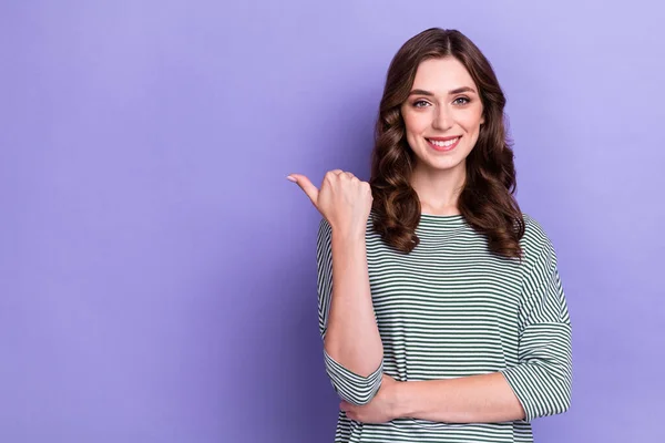 照片上可爱的女孩穿着条纹套头衫 用大拇指指挥空旷的空间广告交易 用紫色背景隔离广告 — 图库照片