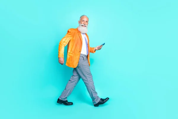 フル長いです写真の面白いです豪華な引退した男のスタイリッシュな衣装歩く空のスペース使用現代的なデバイス隔離されたシアン色背景 — ストック写真