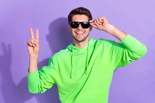 Photo of successful rich positive guy wear green pullover showing v-sign hello chill nightclub star wear sunglasses isolated on violet color background.
