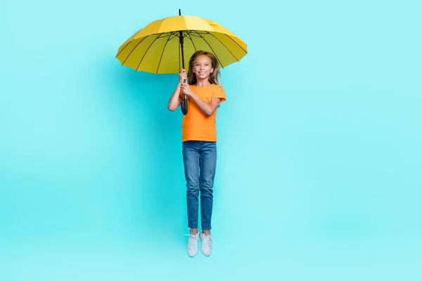 全身上下都是小女孩穿着时髦衣服雨天飞天蹦床带着雨伞的照片 雨伞背景是淡蓝色的 — 图库照片
