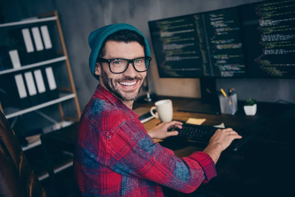 快乐快乐的自由职业者戴着帽子眼镜微笑着在室内工作的现代小玩艺儿在工作场所的阁楼上工作的照片 — 图库照片
