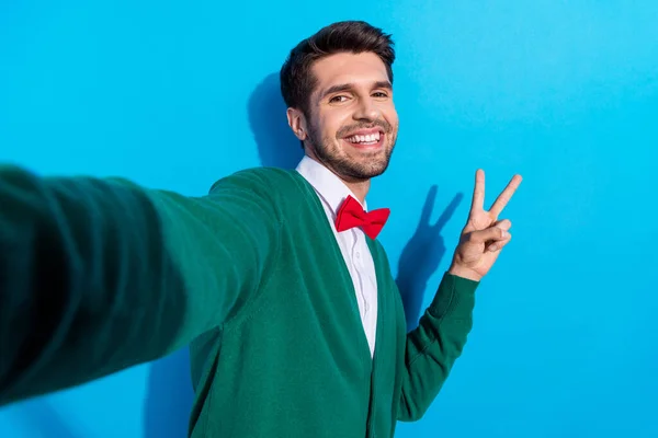 Photo of cheerful attractive man recording video demonstrates v-sign good mood enjoy weekend vacation isolated on blue color background.