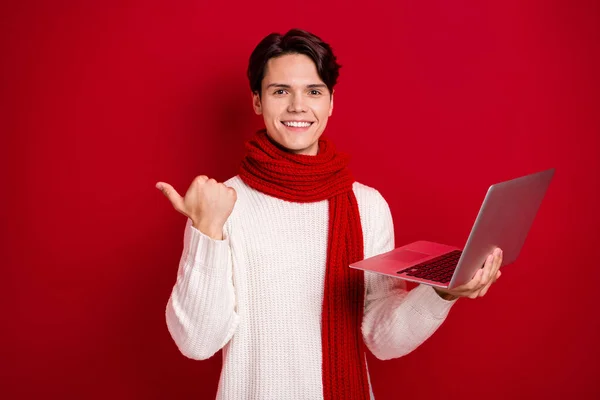 Portrait photo of influencer guy red scarf hold his computer finger point empty space subscribe youtube channel isolated on red color background.