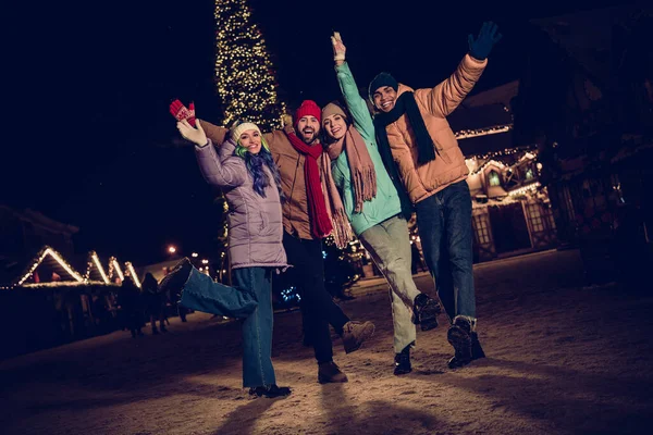 Photo of different funny people wear warm clothes take shot near big decorated fir tree raise hands up want buy more christmas souvenirs outdoors.