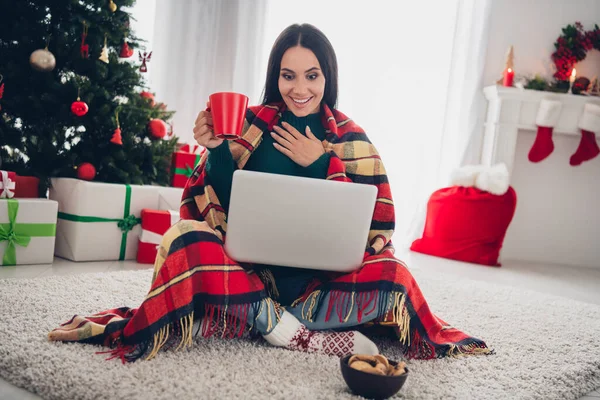 Photo of adorable excited lady dressed knitted x-mas sweater drinking cocoa watching film modern gadget indoors house room.