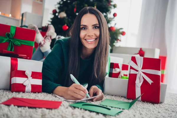 照片上可爱的漂亮女士穿着针织的圣诞毛衣在屋里写着祝福清单 — 图库照片