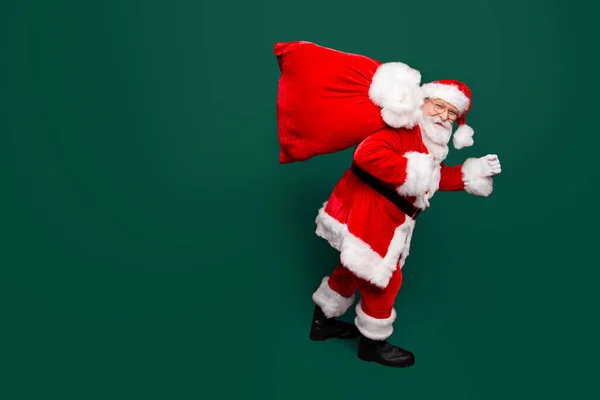 开朗积极的圣诞老人在眼镜手套装备希望你欢快的冬青圣诞举行交付大袋与玩具隔离在明亮生动的红色背景 — 图库照片