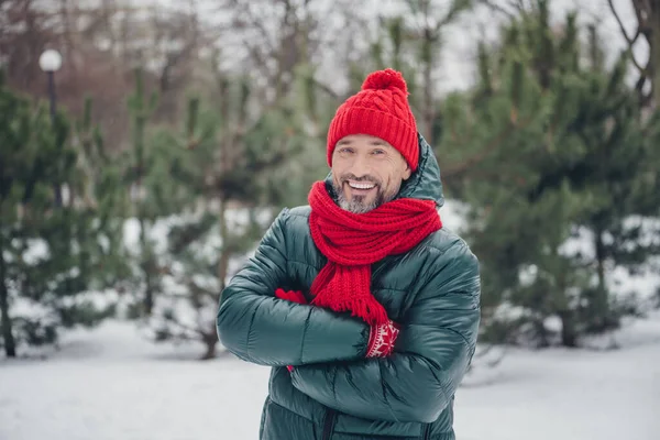 Portrait of satisfied glad person toothy smile crossed arms wear red knitted scarf headwear snowy woods outside.
