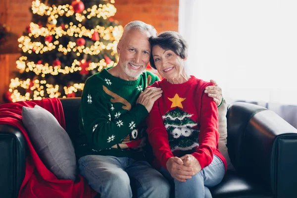 Photo of old age retired couple chill comfortable hug together forever much years love story sitting home sofa near xmas tree garland decor indoors.