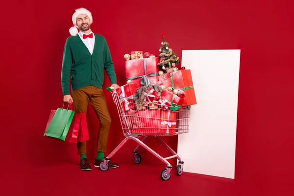 フルボディ写真の紳士男身に着けている緑カーディガン赤蝶近くスーパーマーケットカートスタックギフト近くホワイトバナー隔離された赤の色背景 — ストック写真