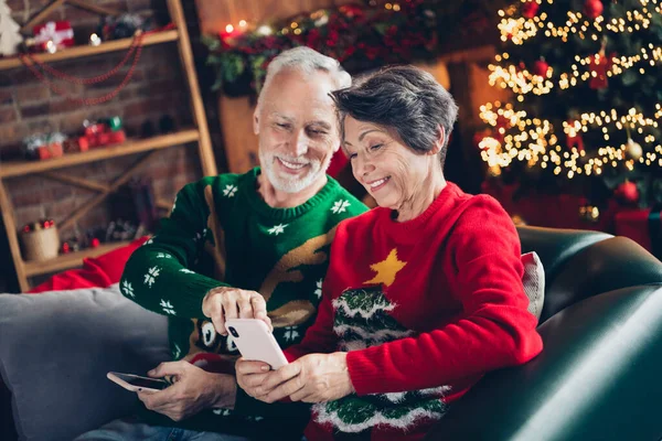 2人の肯定的な美しい高齢者の肖像はソファを使用して座る電話ショップアプリのガーランドライト新年奇跡屋内 — ストック写真
