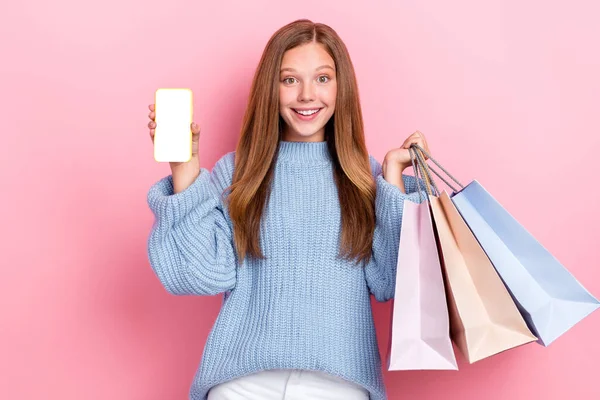 小女孩身穿蓝色针织套头衫 手持购物袋手机 空旷的空间隔离在粉红色的背景下 — 图库照片
